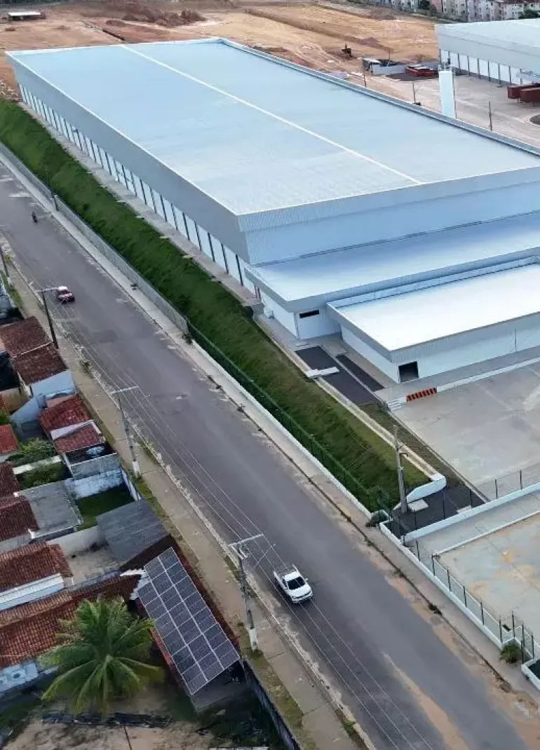 Fachada e pátio de um galpão logístico com telhado metálico e rua de acesso, no Distrito Industrial de Manaus