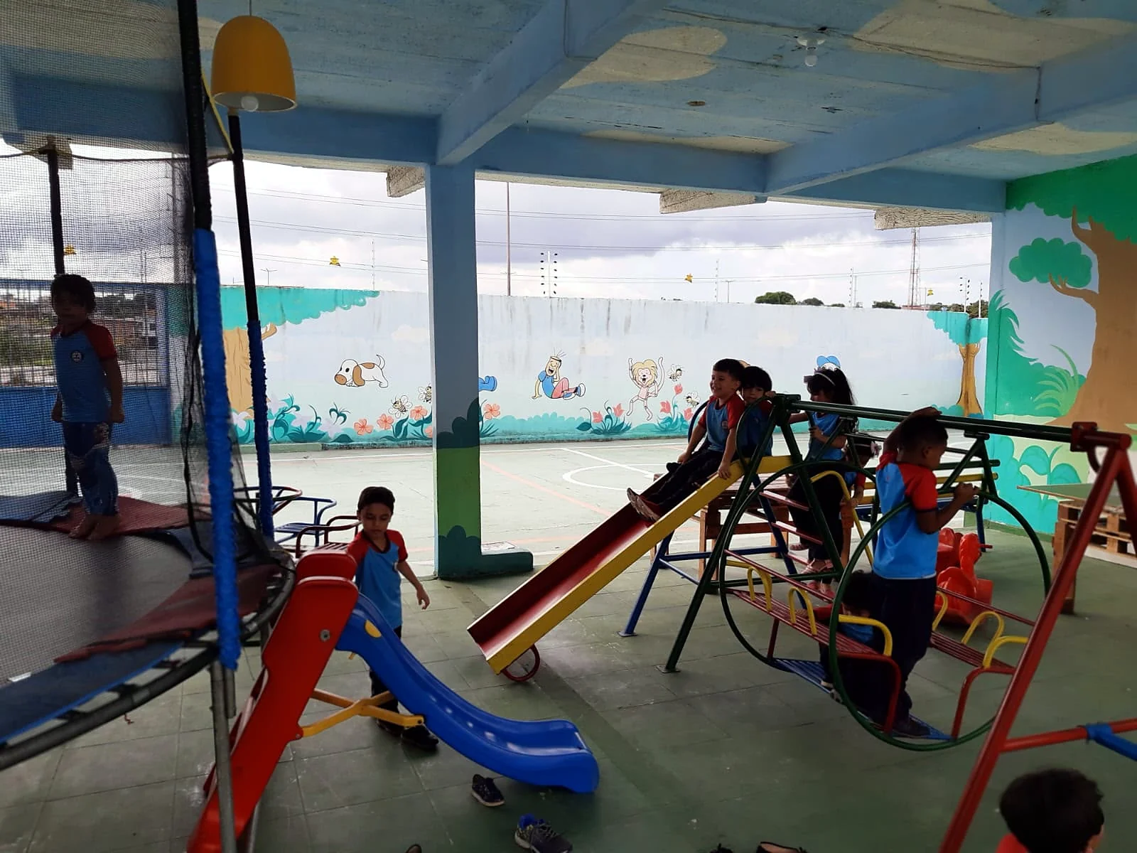Crianças brincando no pátio coberto, com escorregador e gangorra